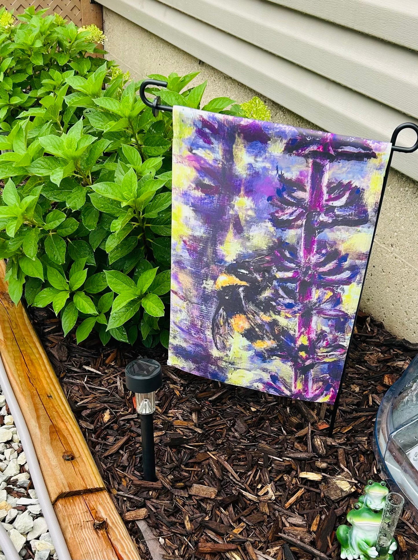 Decorative garden flag with the painting of a bee on purple lavender with green background In a garden setting