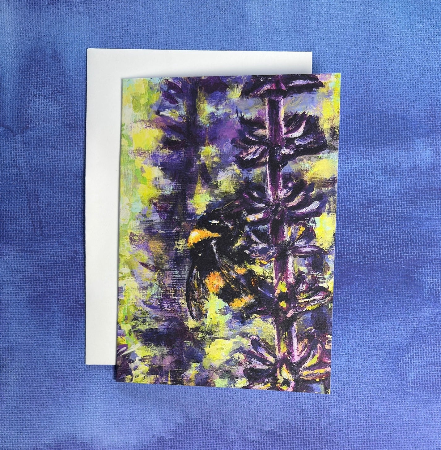 Greeting card with a painting of a bee on a lavender flower on a blue and purple fabric background