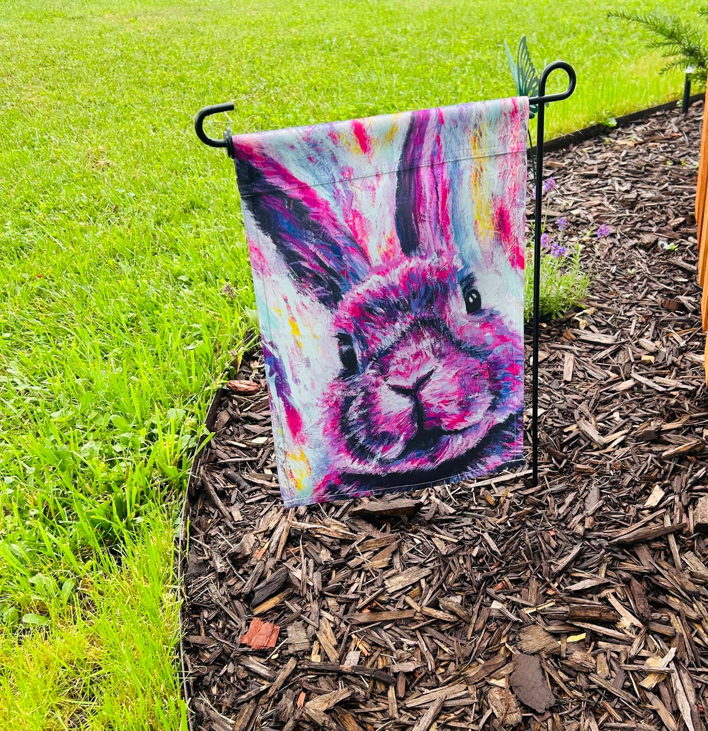 Decorative garden flag with a pink colorful rabbit painting design In garden setting