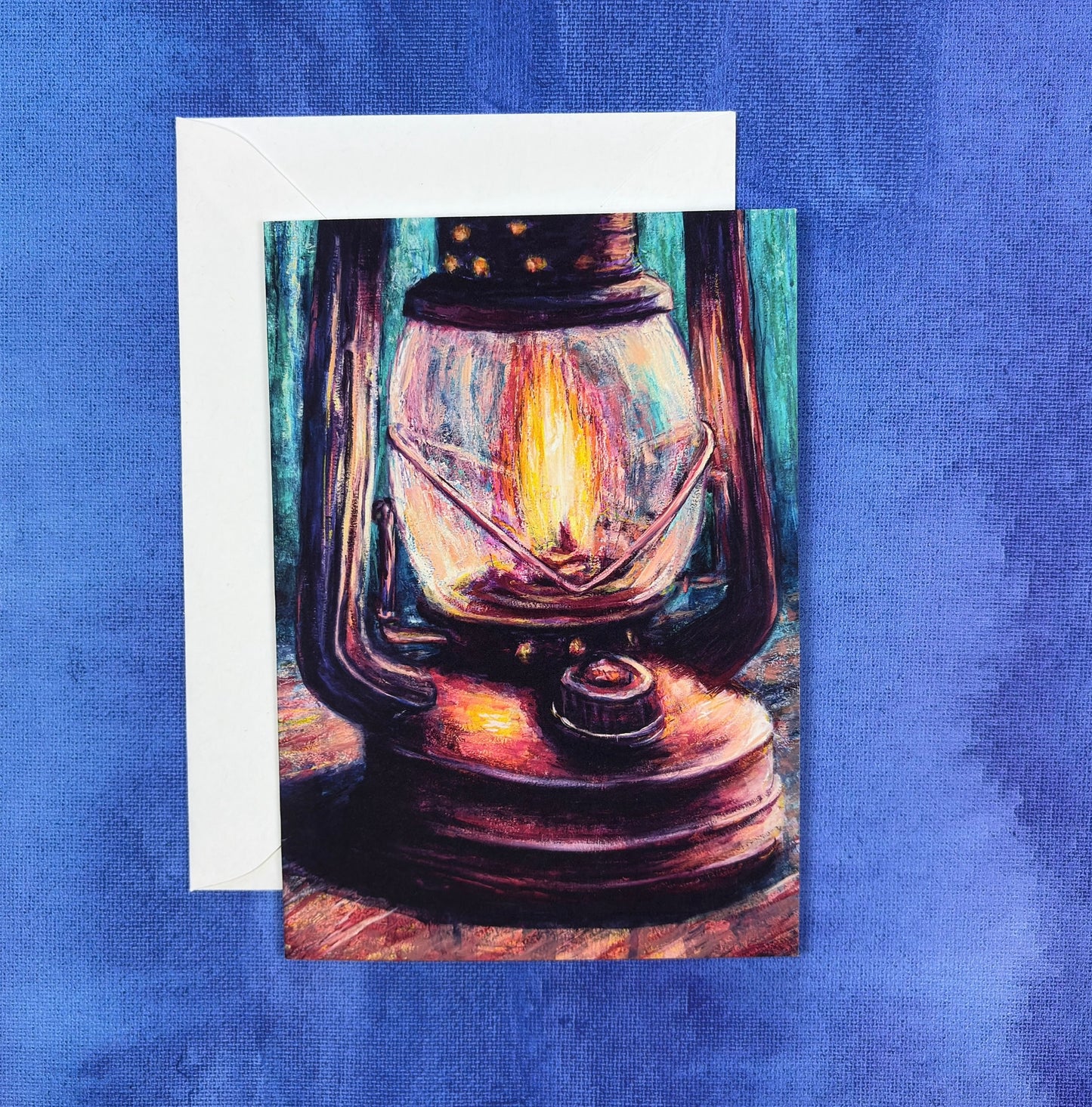 Greeting card with a Painting of a vintage lantern with a glowing light on a camp table with abstract woods in background on a blue textured background