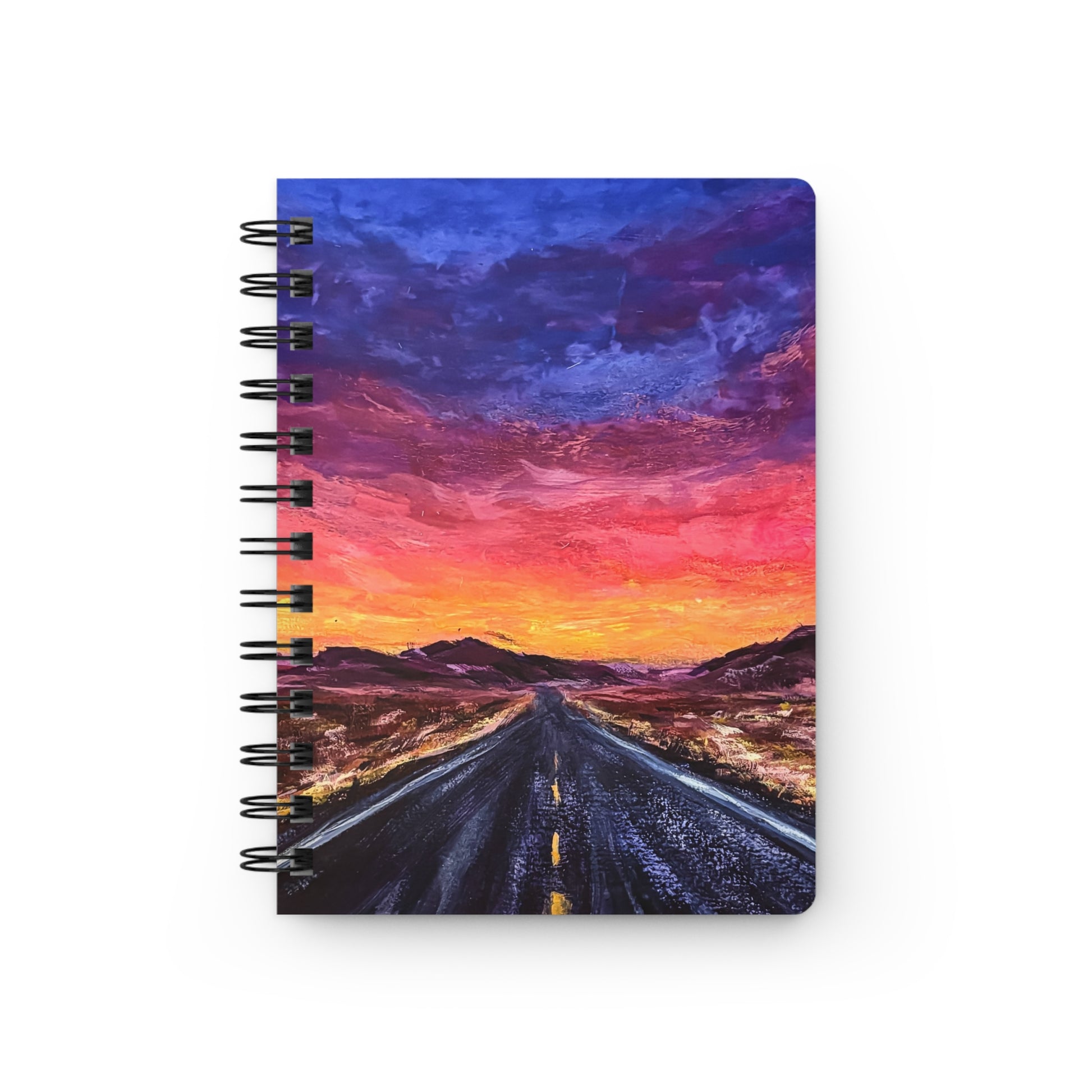 A spiral notebook with a cover depicting a fiery sunset over a desert landscape with a road stretching into the distance.