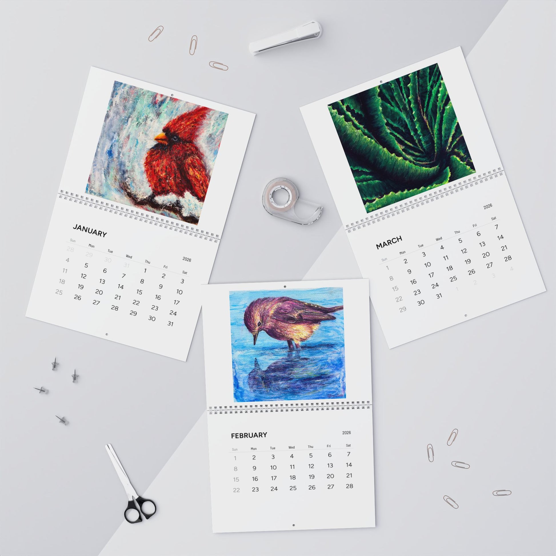 Three calendar pages showing different animals on a gray surface with stationery items.