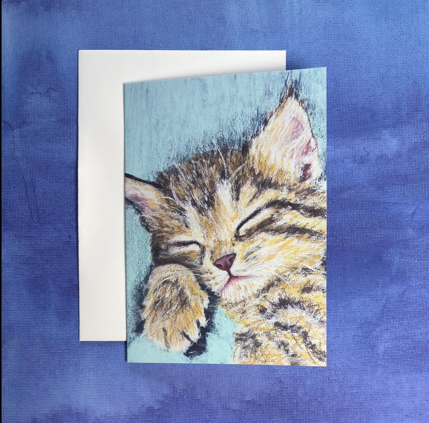 Greeting card with a sleeping kitten painting in the front resting on a blue and purple textured background