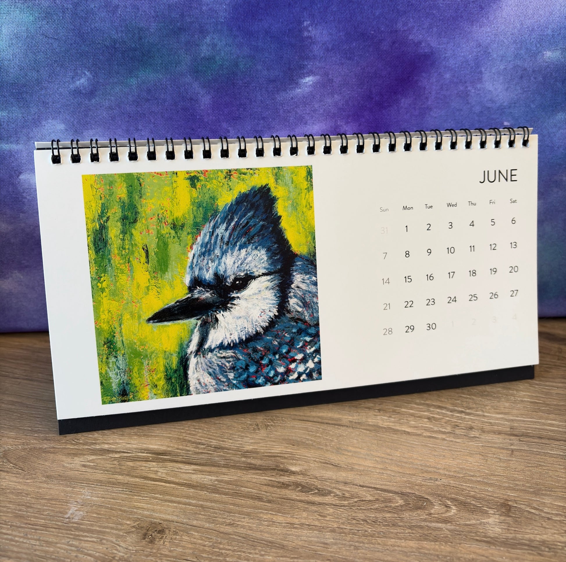 Calendar with a blue jay illustration on a wooden surface and purple background